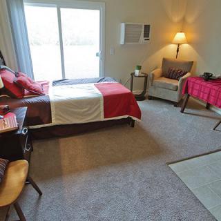 A cozy bedroom with a red and white bedspread, armchair, and desk near a large window.