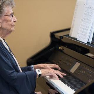 An elderly person playing the piano with sheet music in front of them.