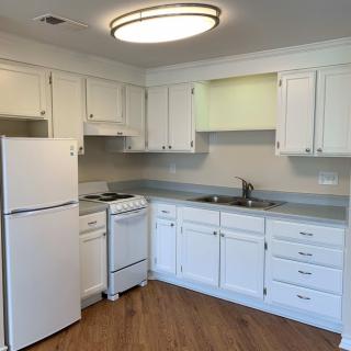 A modern kitchen with white cabinets, featuring a refrigerator, stovetop, and sink.