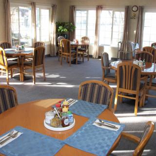 A bright dining room with multiple tables and chairs, featuring neatly arranged place settings.