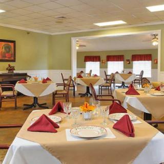 A well-set dining room with neatly arranged tables and chairs, featuring elegant table settings with red napkins.