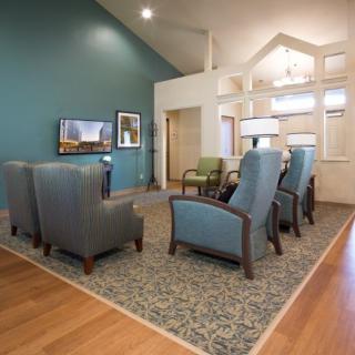 A cozy living room with armchairs facing a television, featuring a patterned carpet and wood flooring.
