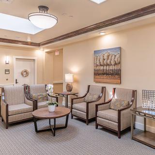 A well-lit waiting room featuring comfortable chairs, a central table, and artwork on the walls.