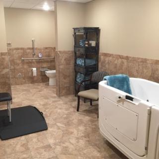 A spacious and accessible bathroom featuring a walk-in tub, tiled flooring, and a comfortable chair.