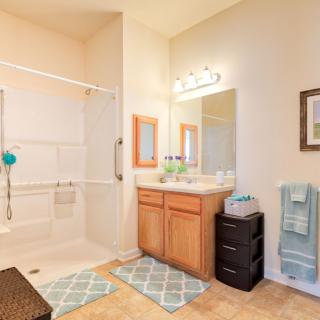 A well-lit bathroom featuring a vanity with mirror, sink, and a shower area.
