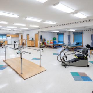 A spacious rehabilitation therapy room equipped with exercise machines and parallel bars.