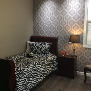 A cozy bedroom featuring a single bed with zebra print bedding, a nightstand with a lamp, and decorative wallpaper.