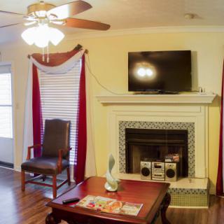 A cozy living room with a fireplace and a television mounted above it, complete with red curtains and a ceiling fan.