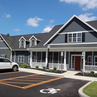 A modern house with a white vehicle parked in the driveway, featuring a neatly marked handicap parking space under a clear blue sky.