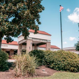A view of a building with an American flag, surrounded by lush greenery under a clear blue sky.