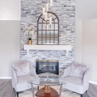 A modern living room featuring a stone fireplace, elegant chandelier, and plush armchairs for a cozy atmosphere.