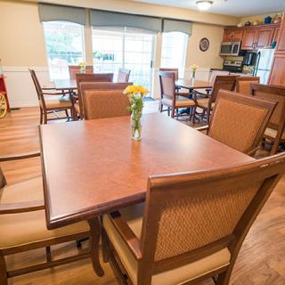 A modern dining area with wooden tables and chairs, featuring a kitchen in the background.