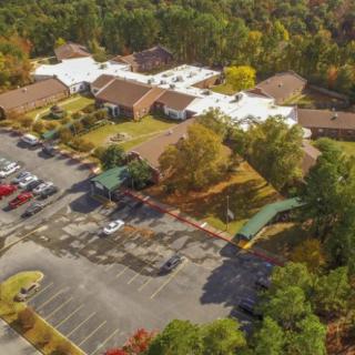 Aerial view of buildings surrounded by trees with a parking lot in the foreground.