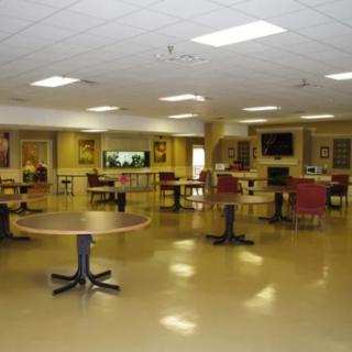 An empty cafeteria with tables and chairs arranged neatly under ceiling lights.