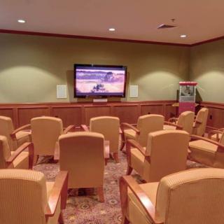 A small theater room with rows of comfortable seating facing a large TV screen, accompanied by a popcorn machine.