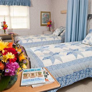 A cozy bedroom with twin beds featuring blue and white quilted covers, complemented by vibrant floral arrangements.