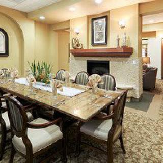 An elegant dining room with a large table, surrounded by chairs and featuring a decorative fireplace.
