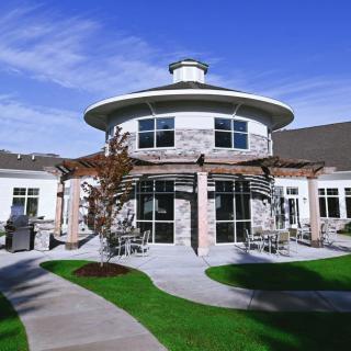 A modern building with a round design and stone facade, surrounded by landscaped gardens under a clear blue sky.