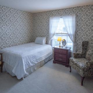 A cozy bedroom with a single bed, vintage wallpaper, and a window letting in natural light.