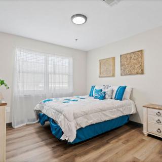 A cozy and minimalist bedroom with a neatly made bed, wooden flooring, and bright natural light coming through the window.