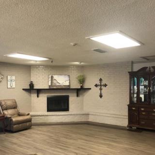 A cozy living room with a fireplace, armchair, and decorative elements including a cross on the wall.