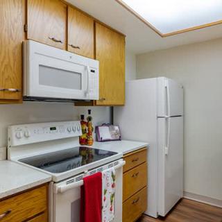 A modern kitchen with wooden cabinets, featuring a stove, microwave, and refrigerator.