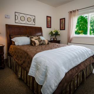 A cozy bedroom with a neatly made bed, decorative artwork, and a bright window letting in natural light.