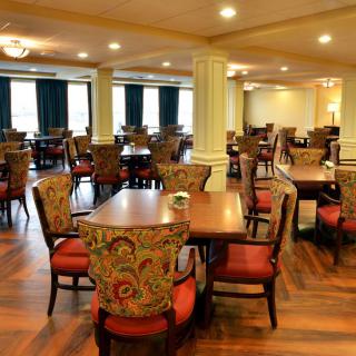 An empty dining room with neatly arranged tables and chairs, featuring a warm wooden floor and soft lighting.