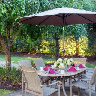 A beautifully set patio table under an umbrella in a lush garden setting.