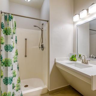A modern bathroom featuring a shower with a tropical-patterned curtain, a sink with a large mirror, and bright lighting.
