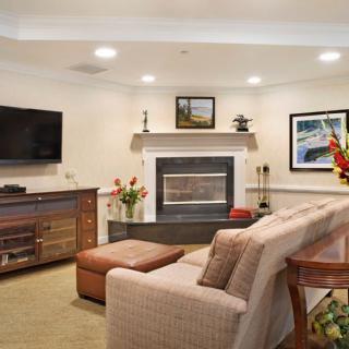 A cozy living room featuring a sofa, fireplace, and television, decorated with flowers and artwork.