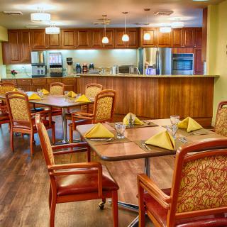 A cozy dining area with neatly arranged tables and chairs, adjacent to a modern kitchen.