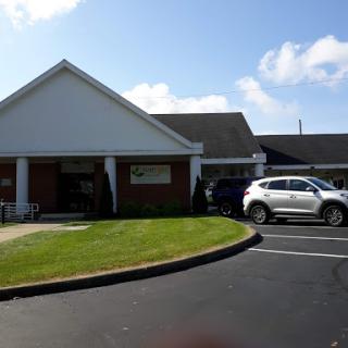 A view of a building with a manicured lawn and parked car under a clear blue sky.