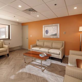A modern living room with beige sofas, an armchair, a wooden coffee table, and wall art on an orange accent wall.