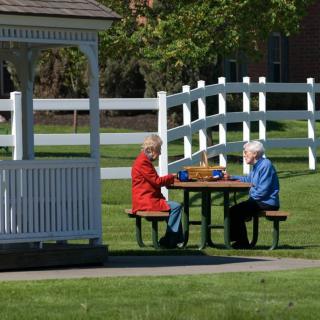 Two seniors enjoying a leisurely game at a picnic table in the park near a gazebo.