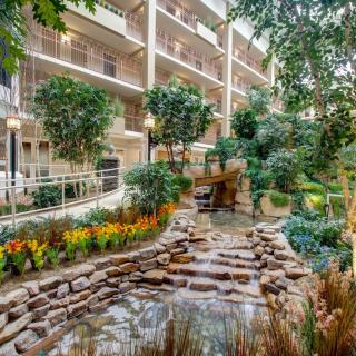 A beautifully designed indoor garden with a water feature in an atrium surrounded by balconies and lush greenery.