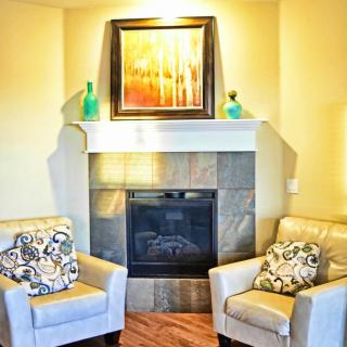 A cozy living room corner with a fireplace, two armchairs, and decorative artwork above the mantel.