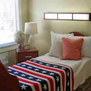 A cozy bedroom with an American flag-themed blanket and a striped pillow on the bed, accompanied by a globe and lamp on the nightstand.
