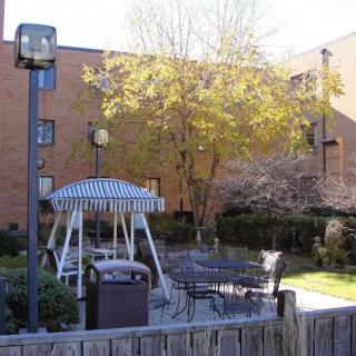 A patio area with a swing, benches, and trees in front of a brick building.