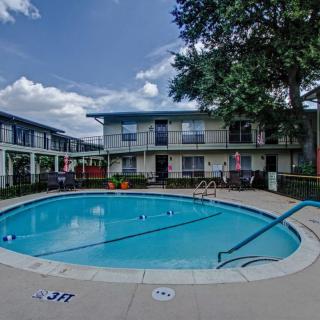 An outdoor swimming pool in the courtyard of a residential apartment complex under a clear blue sky.