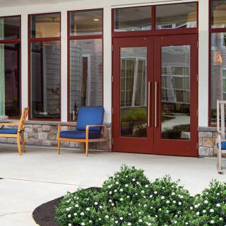 A cozy patio area with chairs and greenery outside a large glass door.