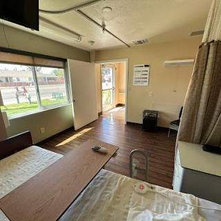 A view of a hospital room featuring beds, a table, and natural light coming through the window.