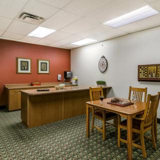 A tidy office with a desk, chairs, and computer setup, featuring a patterned carpet and decorative artwork on the walls.