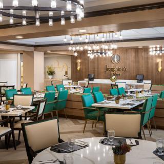 A modern restaurant interior featuring teal chairs, elegant chandeliers, and a warm wood-paneled design.