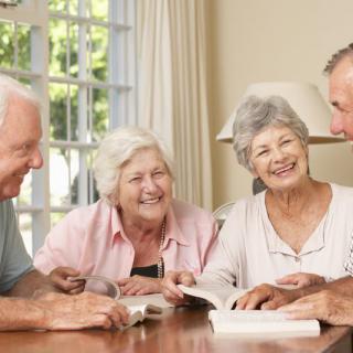 A group of senior friends enjoying a book together indoors, sharing laughter and smiles.