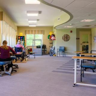 A rehabilitation center therapy room with people exercising and various exercise equipment.