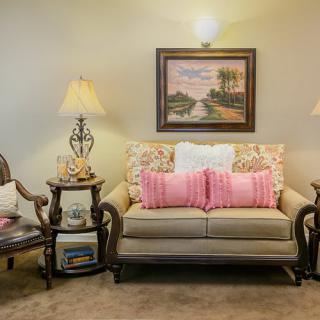 A cozy living room with a sofa adorned with pink pillows, flanked by decorative lamps and side tables, and a landscape painting on the wall.