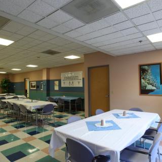 A spacious dining area with neatly arranged tables and chairs, featuring colorful tiled flooring and decorative wall art.