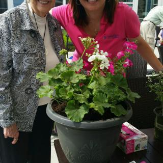 Two individuals smiling next to a potted flower arrangement.