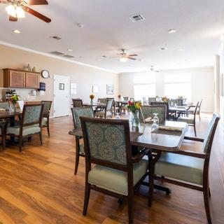 A bright and cozy dining area with wooden floors, multiple tables and chairs, and ceiling fans, illuminated by natural light.